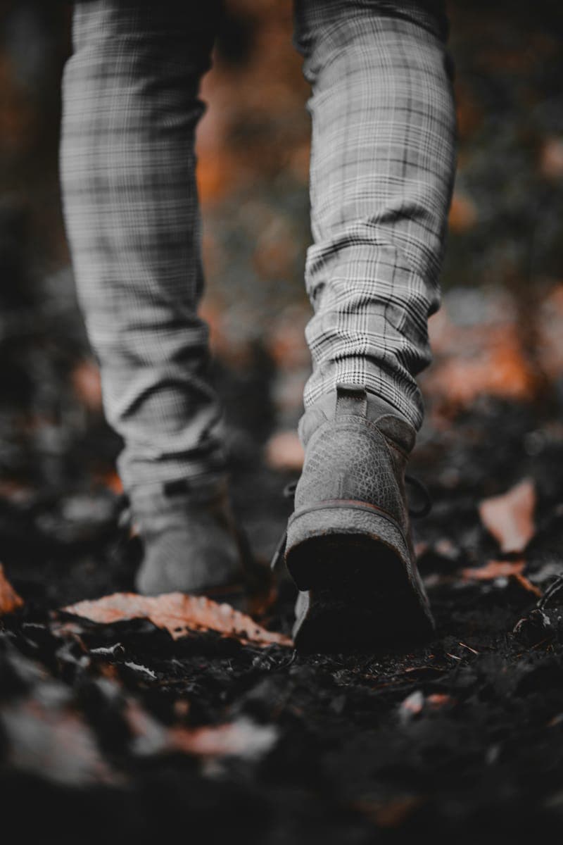 Close-up of checked trousers and suede boots walking over autumn leaves
