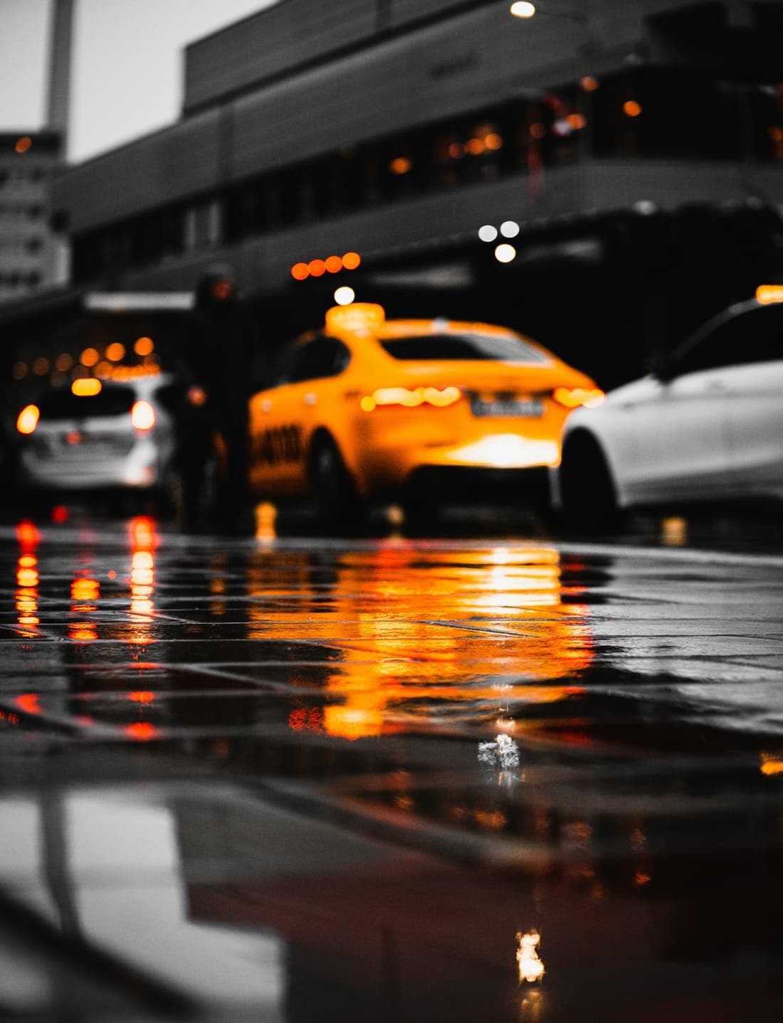 A yellow taxi and city lights reflected on a wet street at dusk
