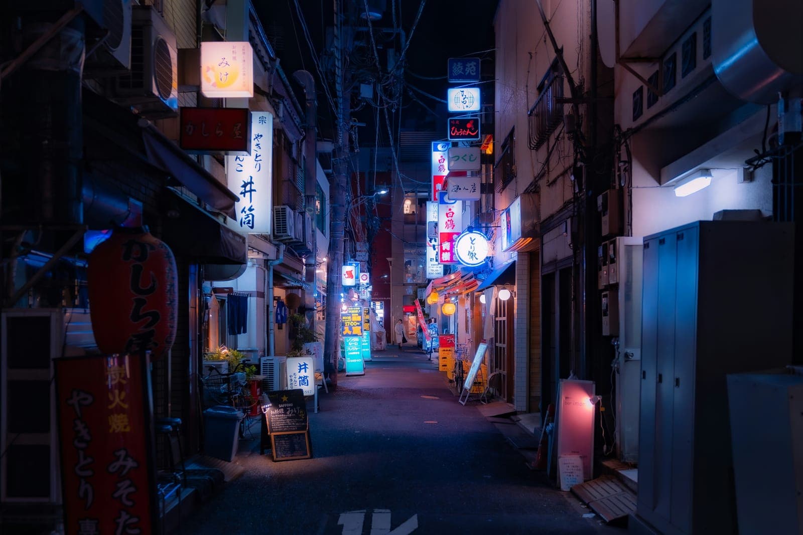 A narrow city street lit by neon signs at night